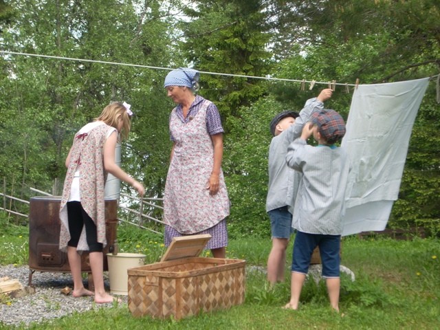 Barn och ledare i 1930-talskläder hänger tvätt utomhus
